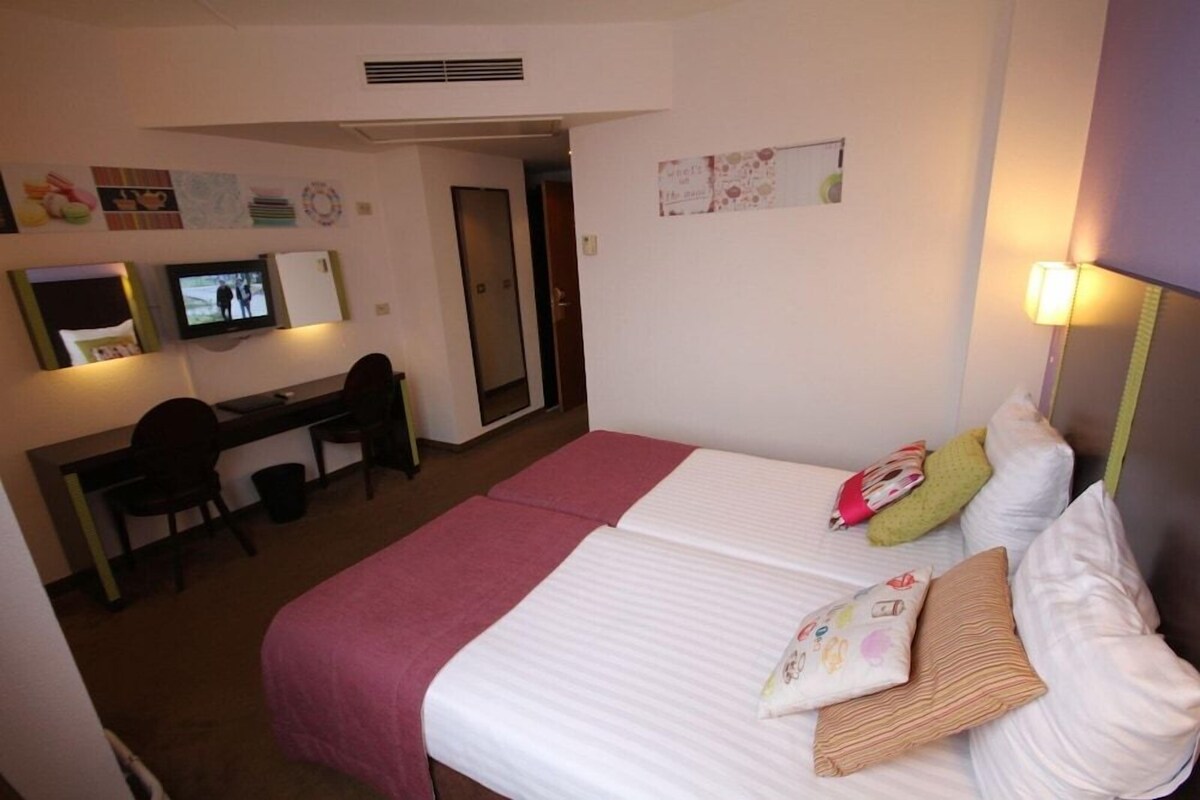 Una camera d'albergo con due letti, una scrivania, una sedia, una televisione e uno specchio.