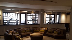 A modern living room with a sectional sofa, a round ottoman, and a large window with decorative vases. - Floris Arlequin Grand Place (Brussels)