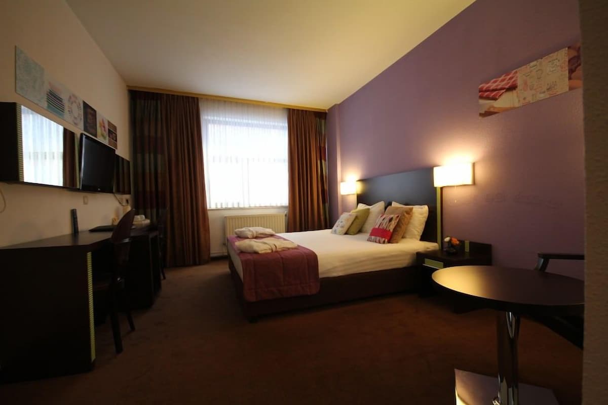 Una habitación de hotel con cama, escritorio, silla y una pequeña mesa.