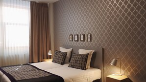 A neatly made bed with patterned pillows, a bedside table with a lamp, and a patterned wall. - Floris Arlequin Grand Place (Brussels)
