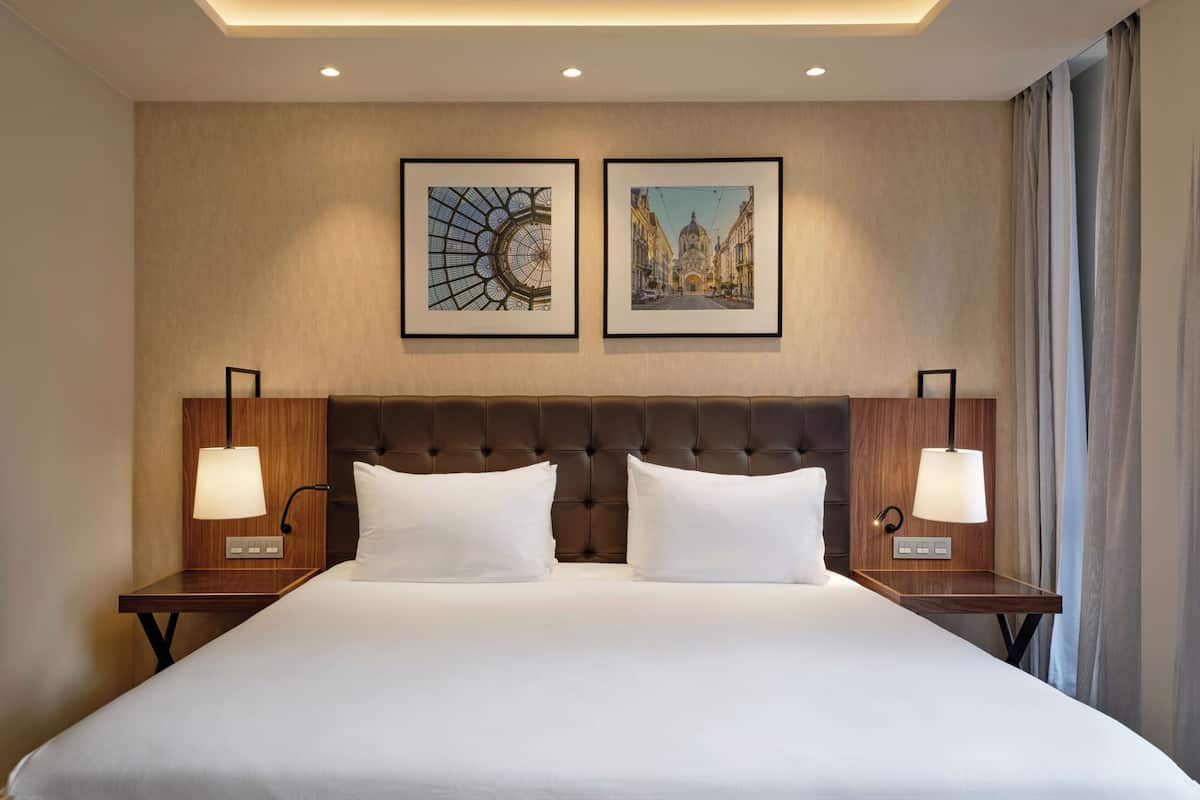 A hotel room with a large bed, two wall-mounted lamps, and two framed pictures above the bed.