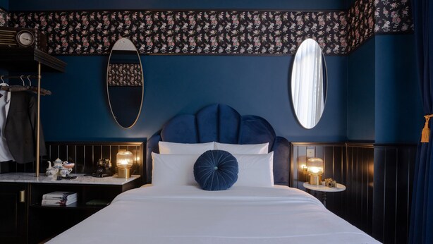 Un dormitorio con cama, cómoda, espejo, reloj y una pared con estampado floral.