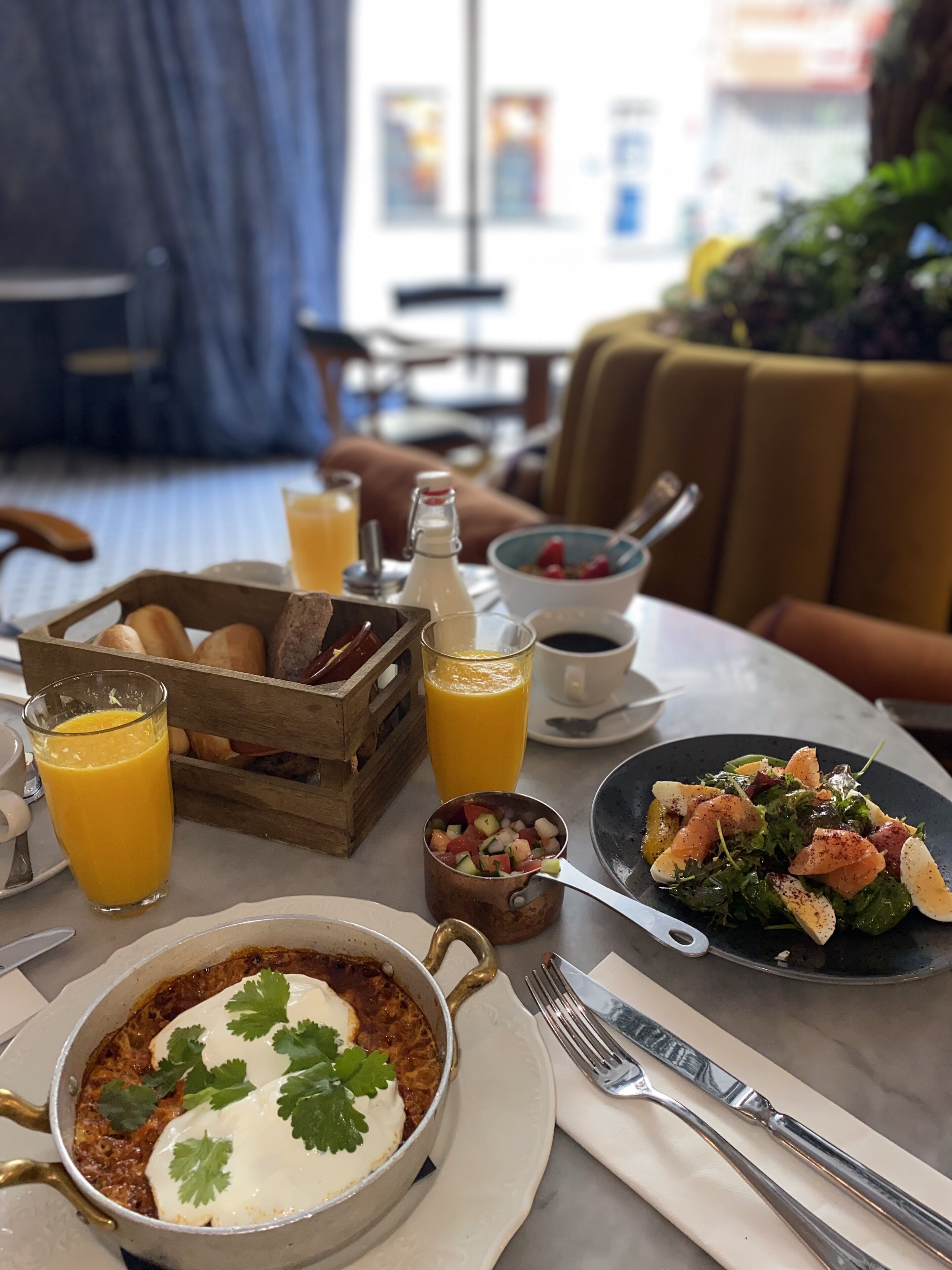 A breakfast setting with a variety of dishes, including a bowl of cereal, a plate of salad, and a pot of soup garnished with cilantro. There are also glasses of orange juice and a bottle of milk on the table.