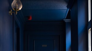 Una puerta azul oscuro con el número 228, un picaporte de latón y una lámpara fijada a la pared.