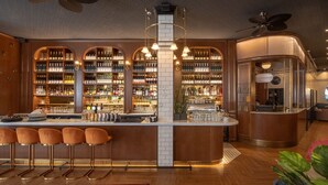 Zona de bar con mostrador, taburetes y estantes llenos de botellas y vasos.