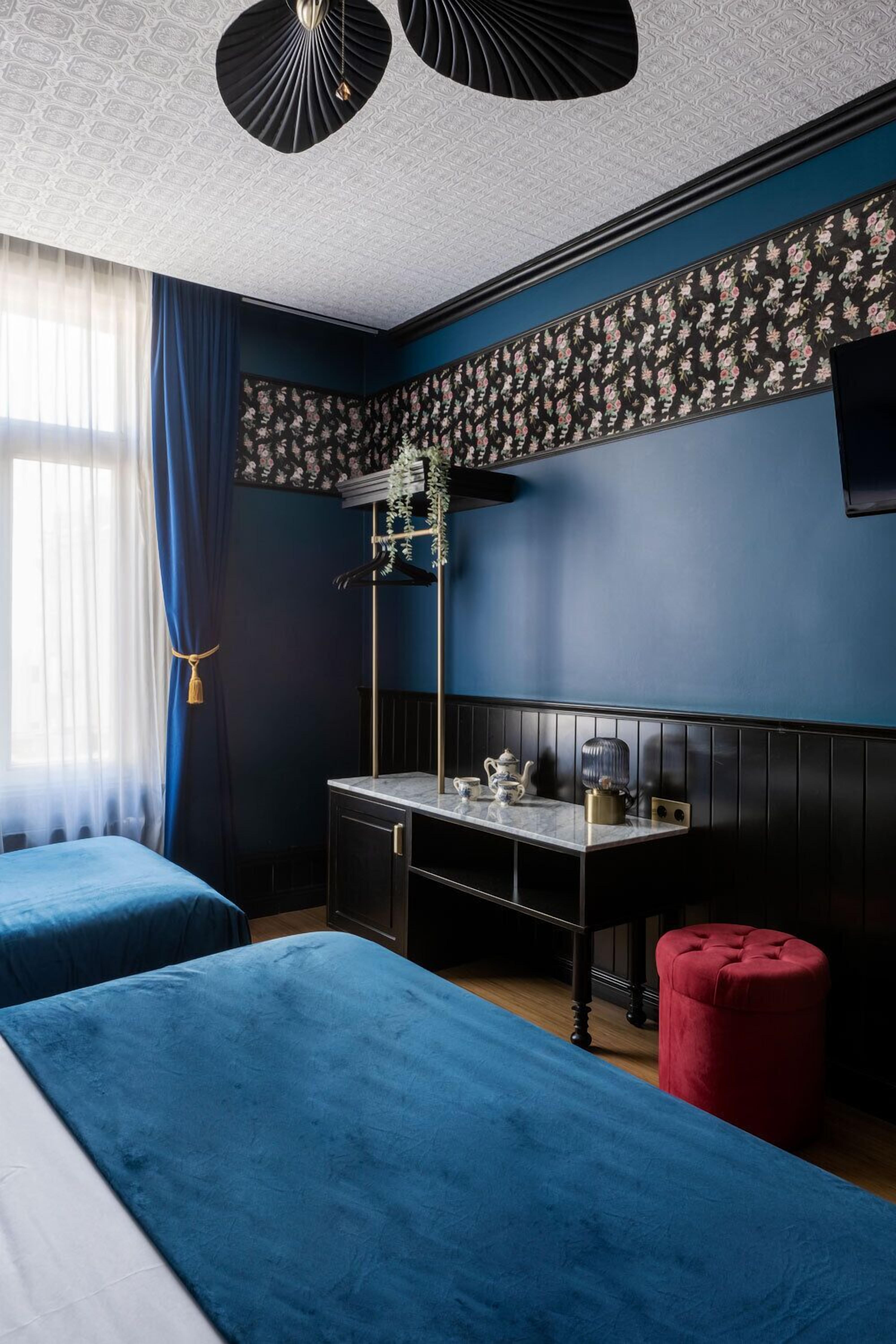 Een kamer met twee bedden, een bureau met lamp, een rode poef en een tv aan de muur.
