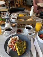 Una escena de desayuno con un plato de comida, una jarra de leche, una jarra de jugo de naranja y un recipiente pequeño de mermelada.