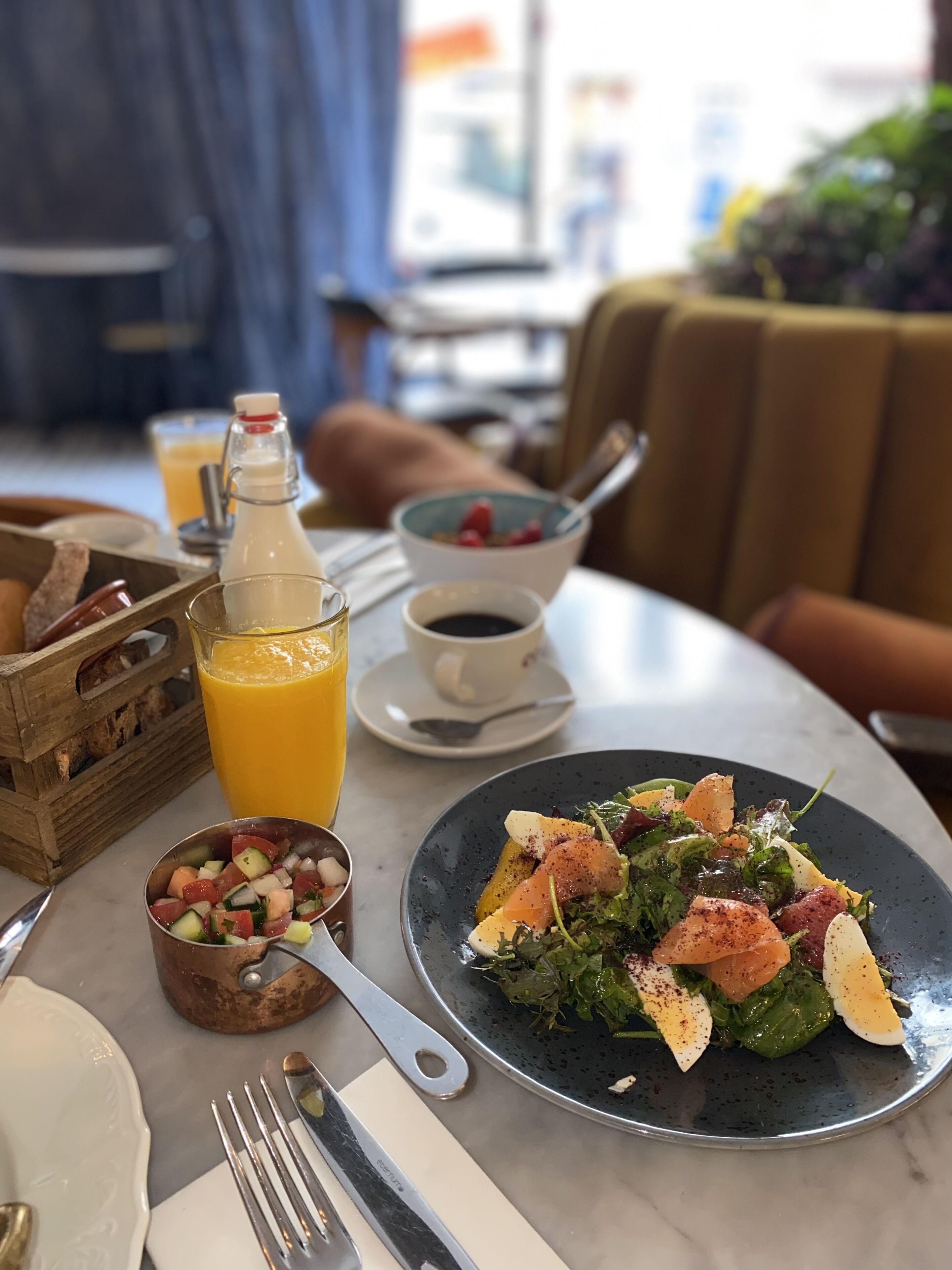 A dining table with a salad, a glass of orange juice, a coffee cup, and a bread basket.