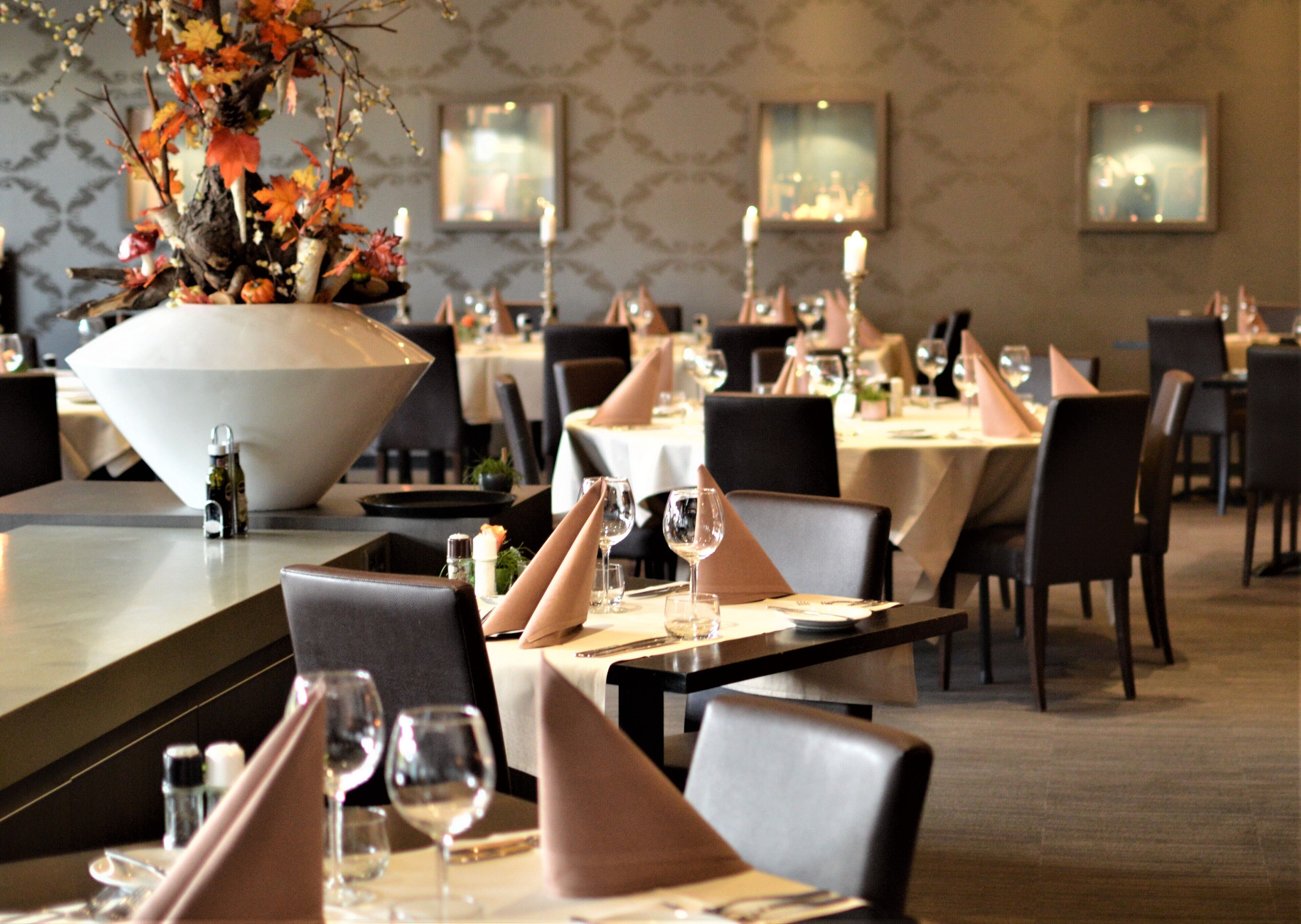 A restaurant with tables set for dining, featuring a large floral centerpiece and candle holders.