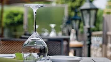 Une table avec un vase en verre transparent, une serviette verte et une assiette, disposée à l’extérieur, avec en arrière-plan une végétation floue et un lampadaire.