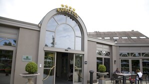 En hotellentrén med en stor, välvd dörröppning, en skylt med texten ”EUROTEEL” och en sittgrupp med bord och stolar utomhus.