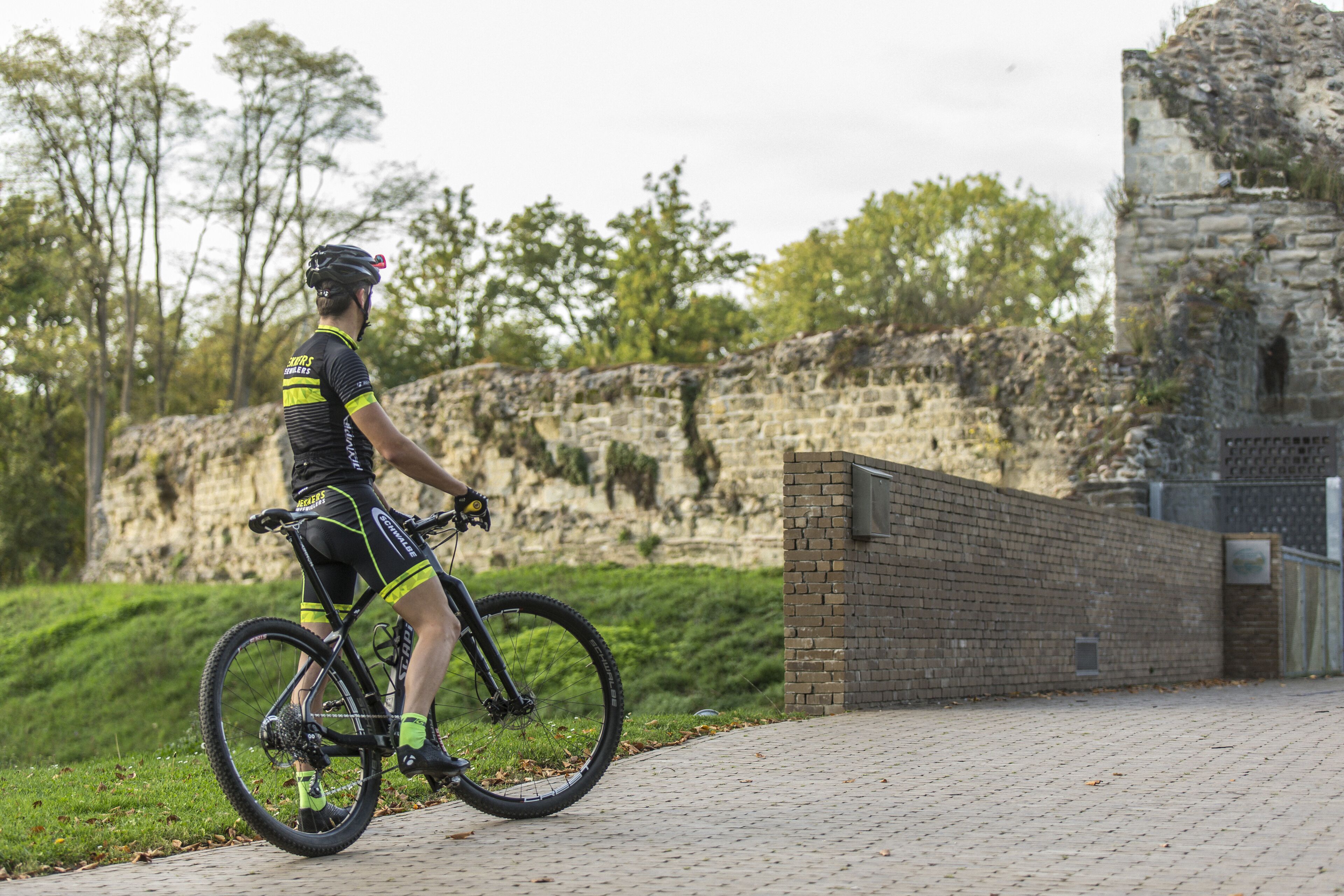 A cyclist on a paved path with a stone wall and greenery in the background.