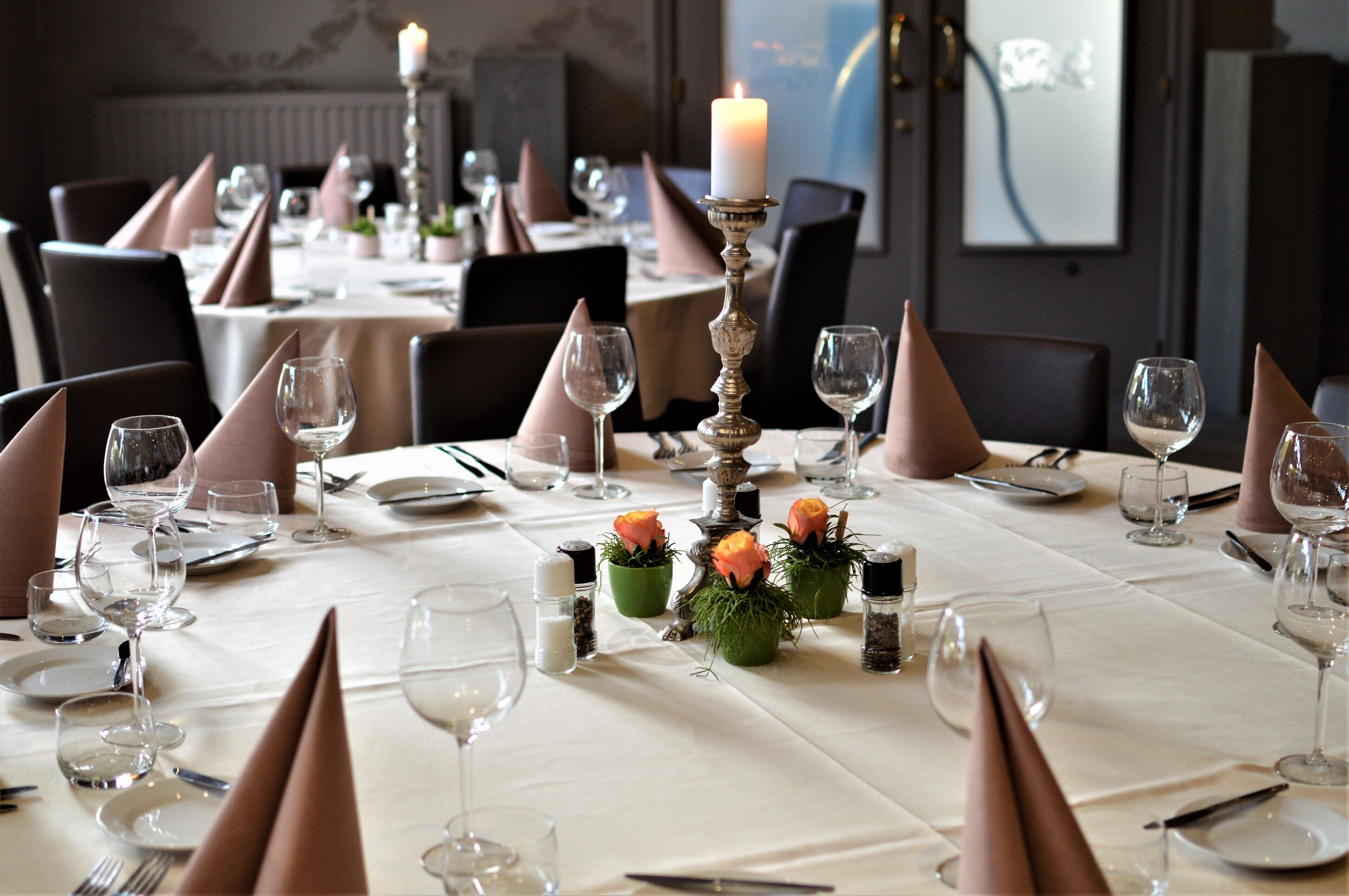 Een eettafel gedekt met een witte tafelkleed, roze servetten en kaarsen.