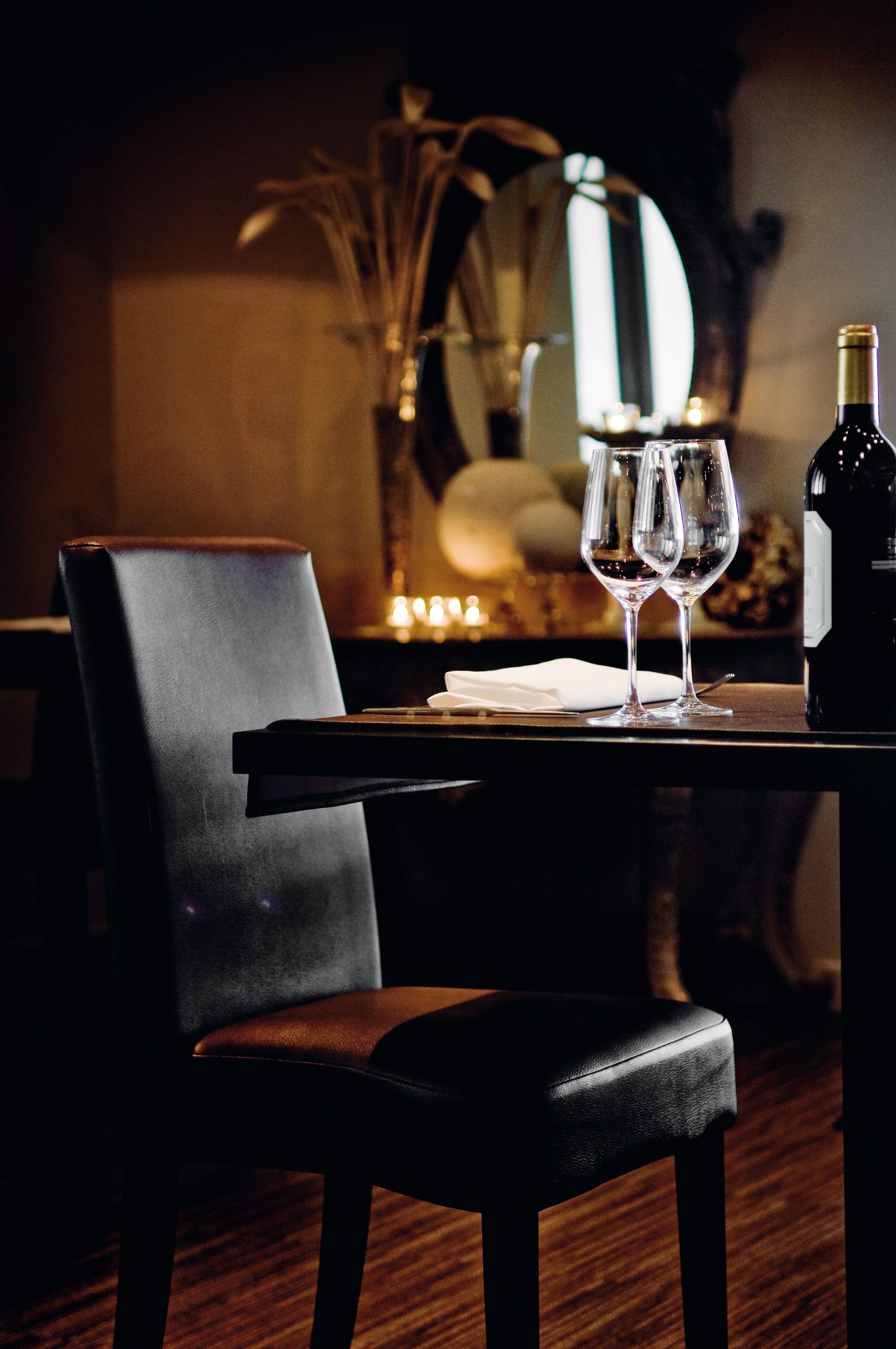 A dining table with two wine glasses and a bottle, a chair, and a mirror in the background.
