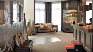 En modern hotellobby med en soffa, ett soffbord, en bardisk med en bärbar dator och ett stort fönster med gardiner.