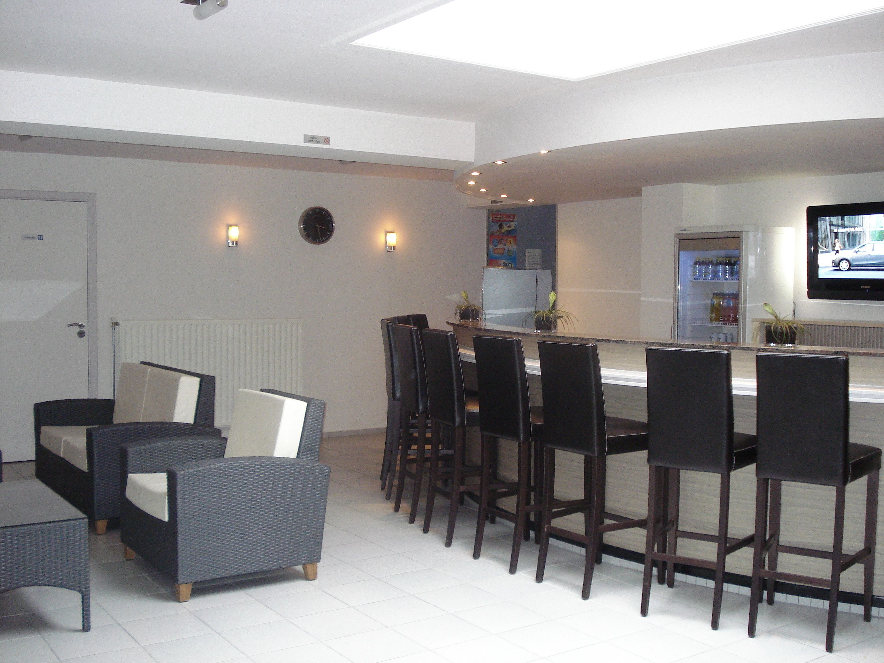 A modern kitchen with a bar area, equipped with bar stools, a refrigerator, and a television.