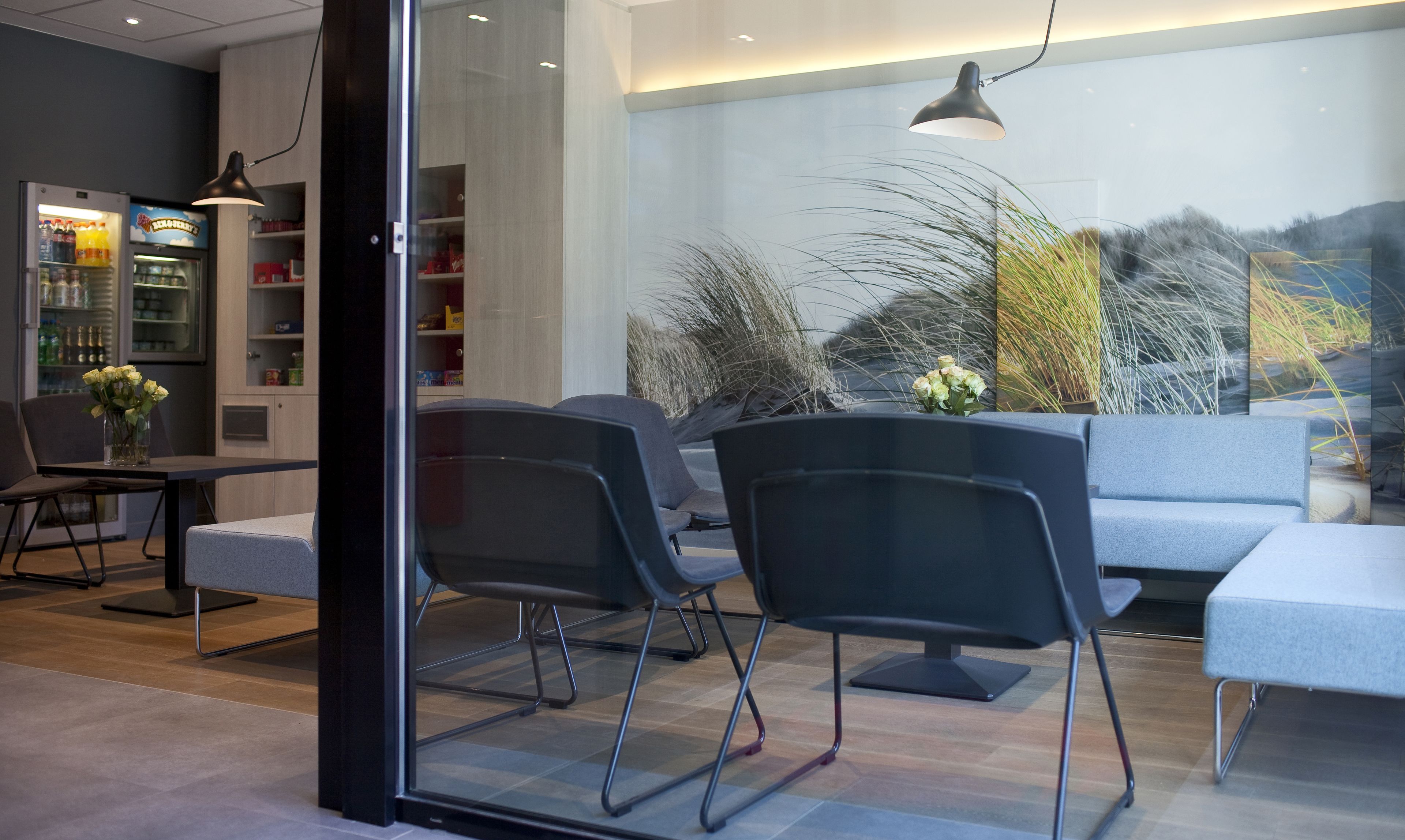 Un intérieur moderne avec une cloison en verre, un coin repas comprenant des chaises et une table, et un réfrigérateur rempli de boissons.