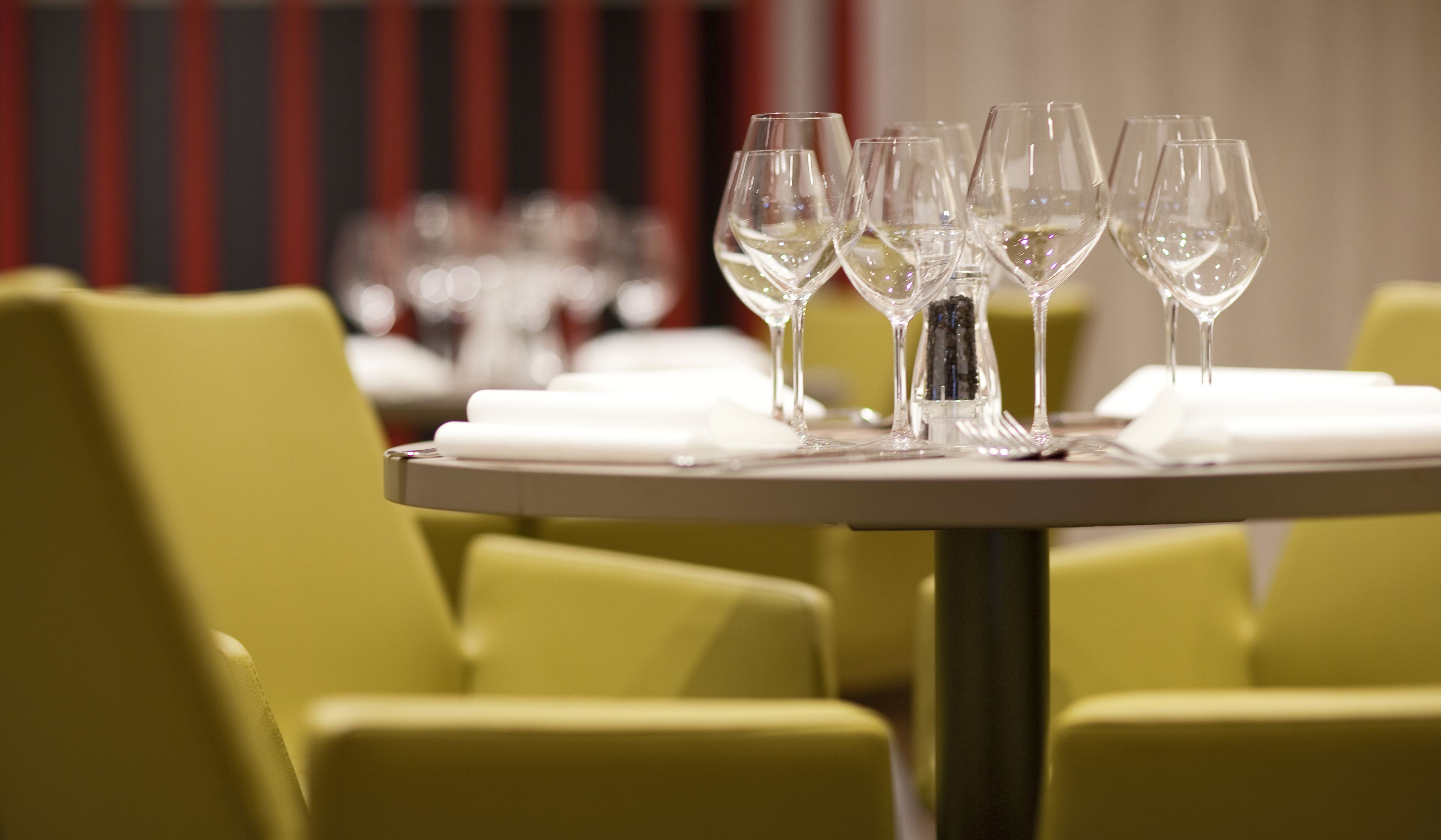 A dining table with multiple wine glasses and plates, set against a backdrop of yellow chairs and a striped wall.