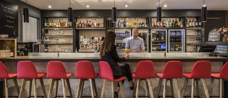 Zona de bar con sillas rojas, un barman y estantes llenos de botellas y copas.