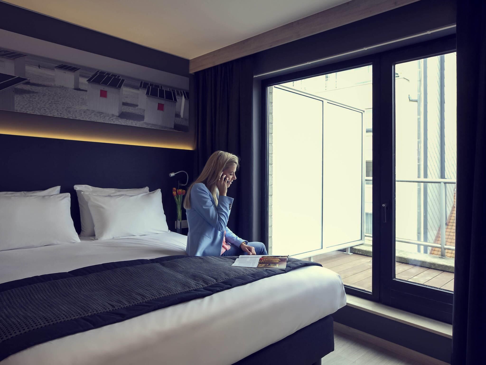 Een moderne hotelkamer met een groot bed, een bureau en uitzicht op de stad door een groot raam.