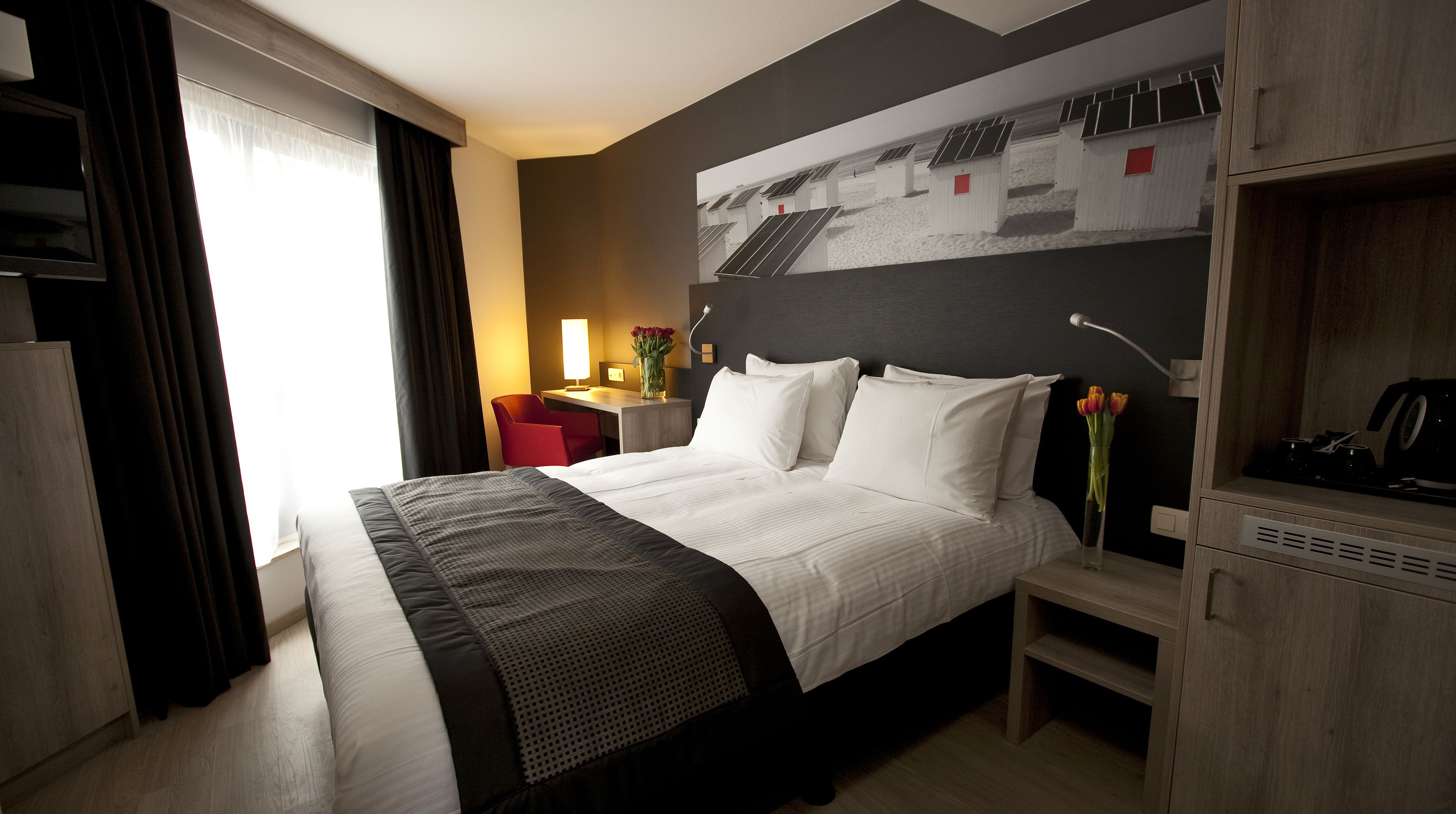Habitación de hotel con cama, escritorio, silla, televisión y estante en la pared.