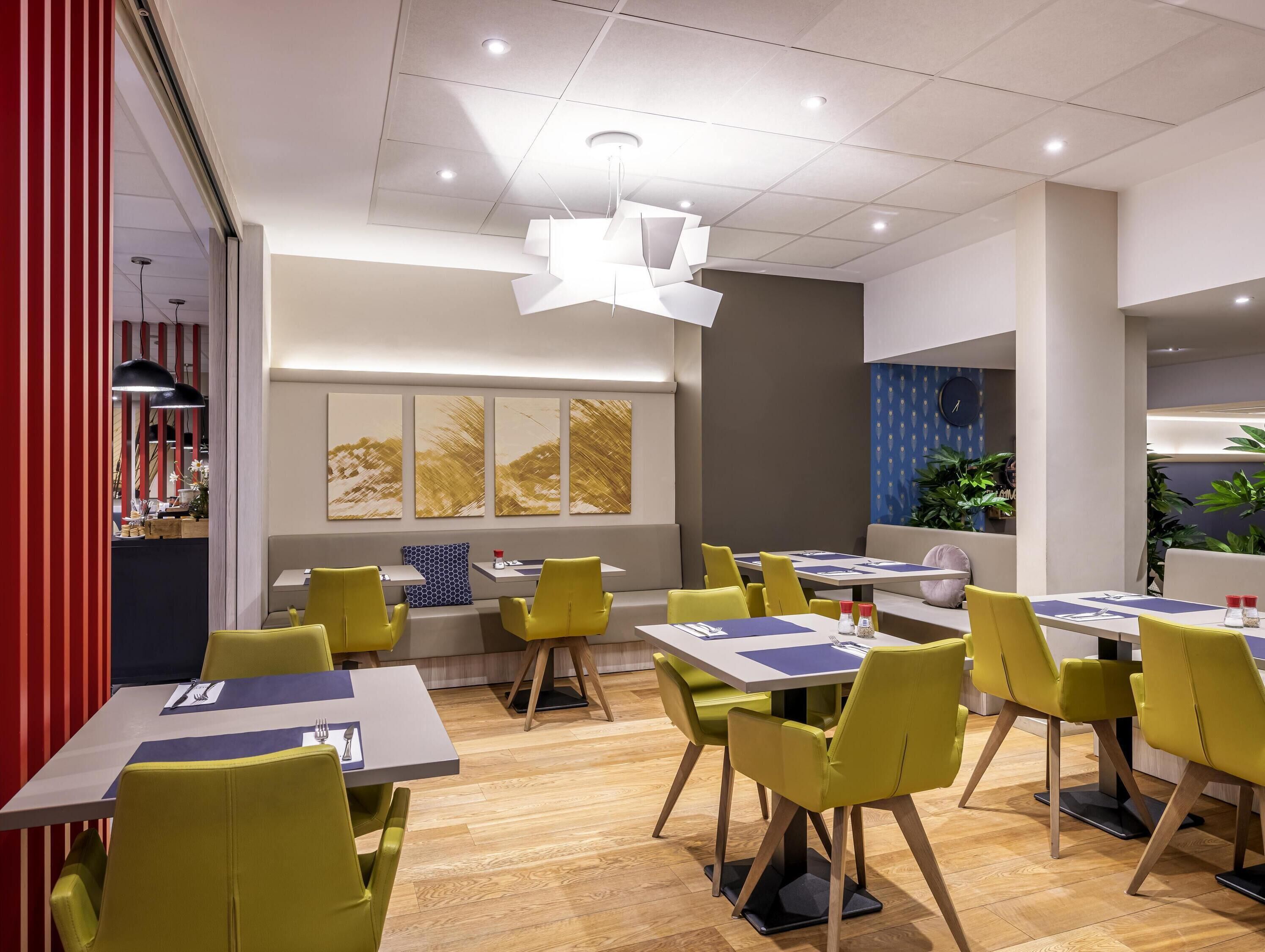 A modern dining area with yellow chairs, white tables, and a central light fixture.