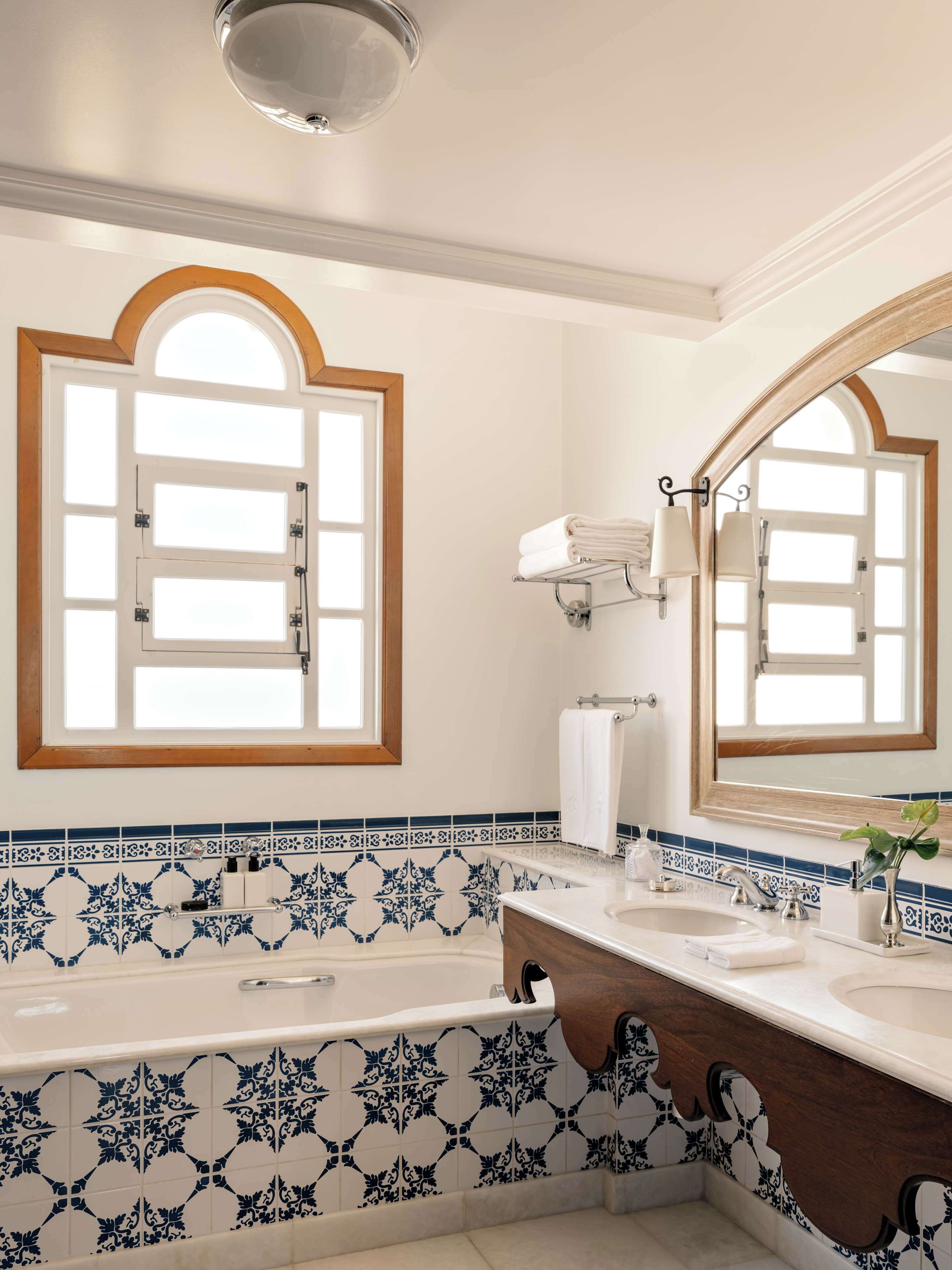 A bathroom with a bathtub, two sinks, a large mirror, and a window with a wooden frame.