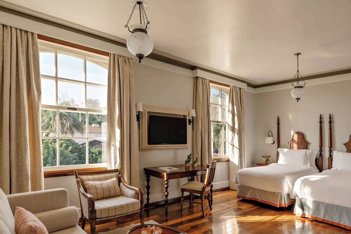 A hotel room with a sofa, two beds, a desk, and a TV.