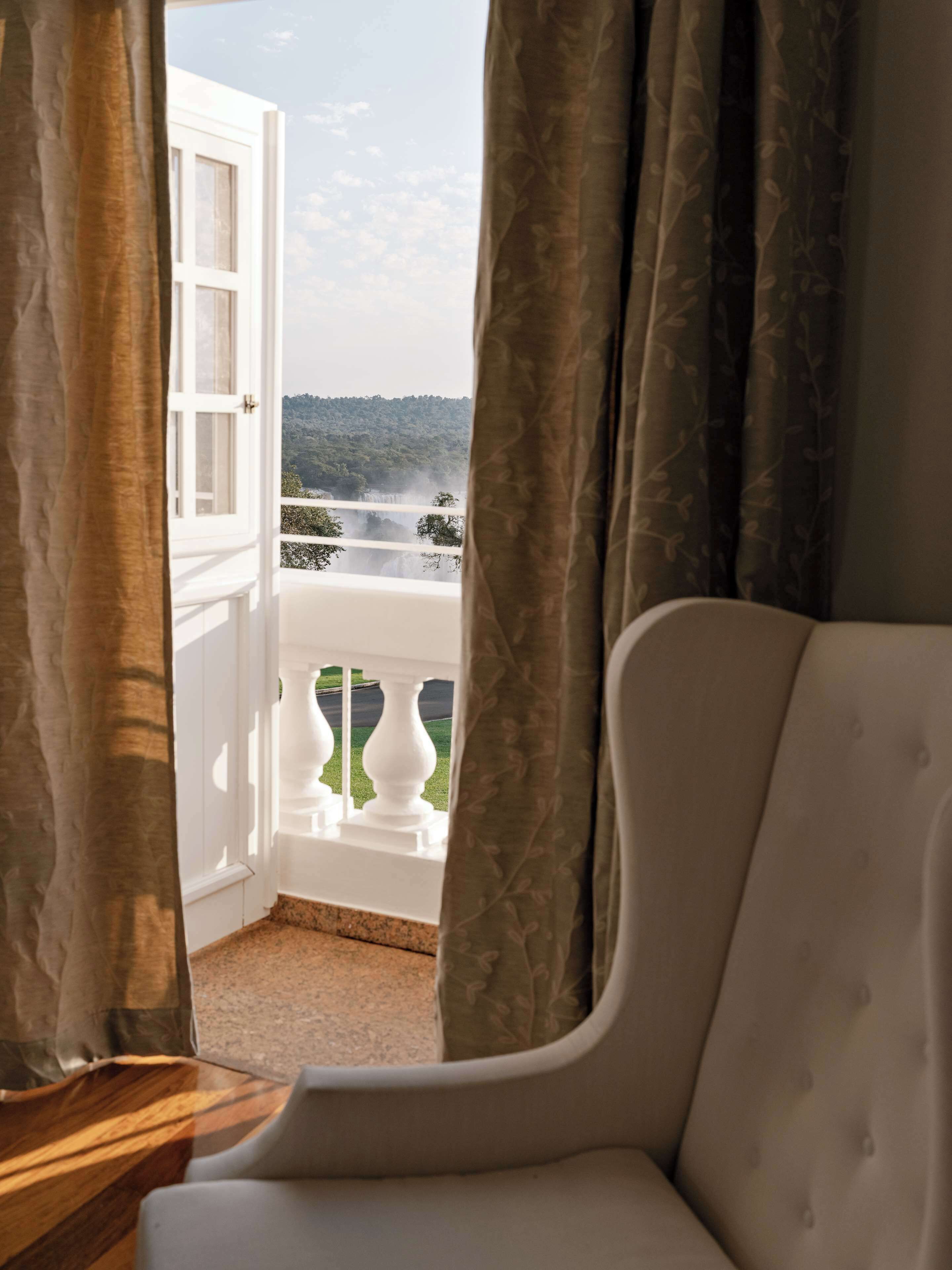 A room with a view of a waterfall and greenery through an open window.