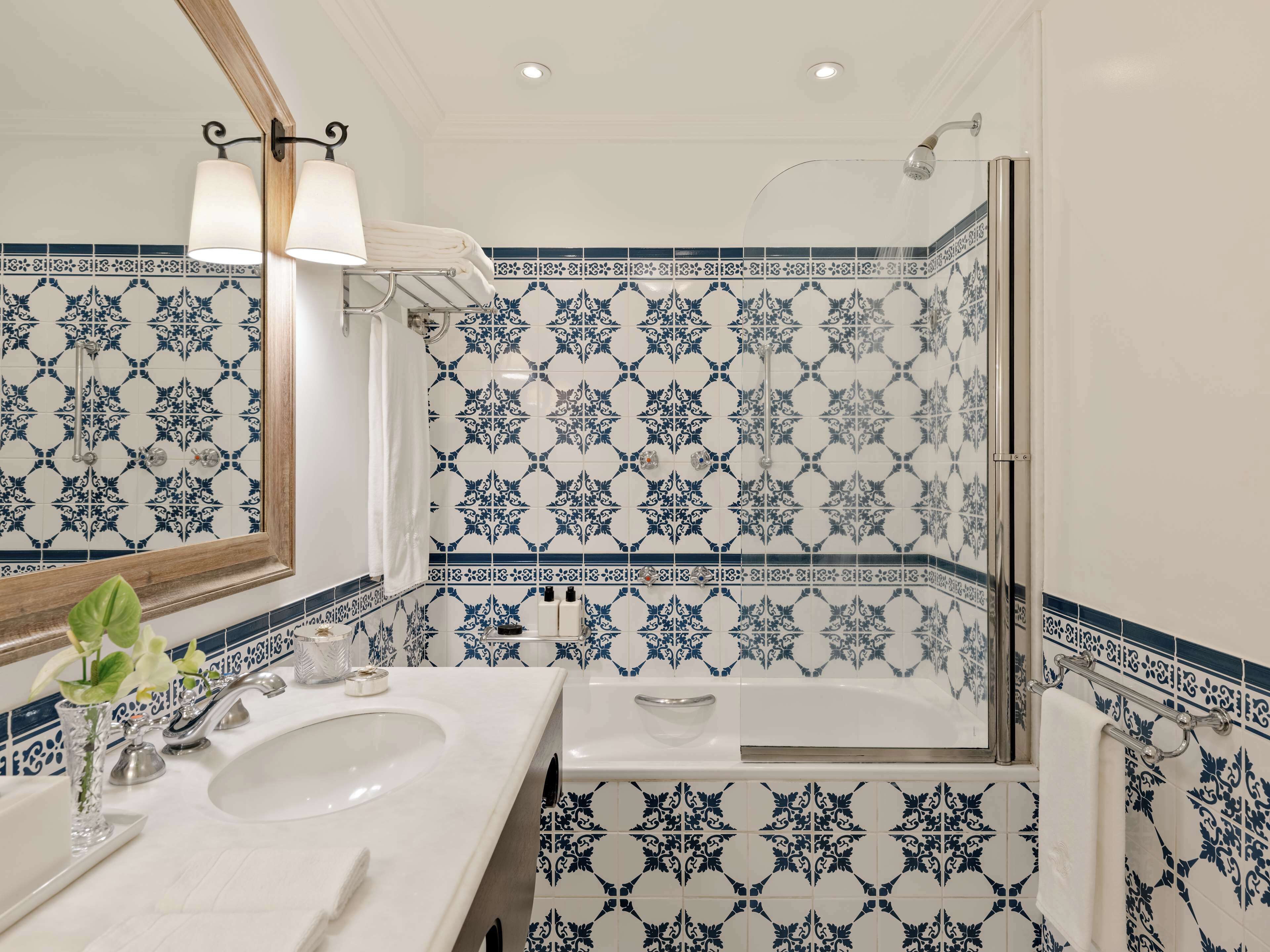Une salle de bain avec un lavabo blanc, un miroir et une douche dont les carreaux sont ornés de motifs bleus et blancs.