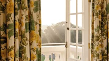 Una habitación con una puerta blanca, cortinas florales y vistas al exterior con vegetación.
