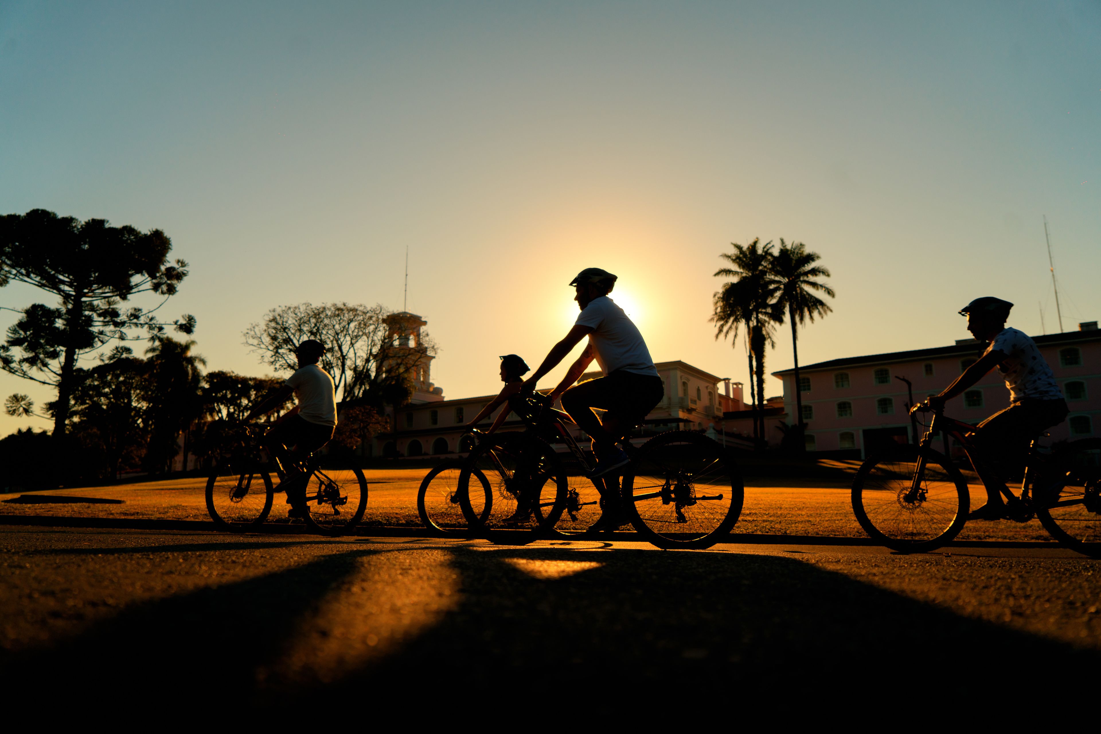 Drie fietsers rijden over een weg, met een zonsondergang op de achtergrond.