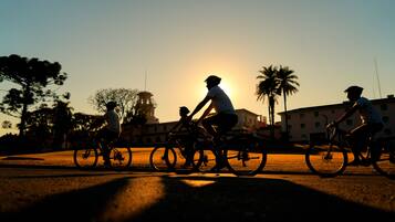Drie fietsers rijden over een weg, met een zonsondergang op de achtergrond.