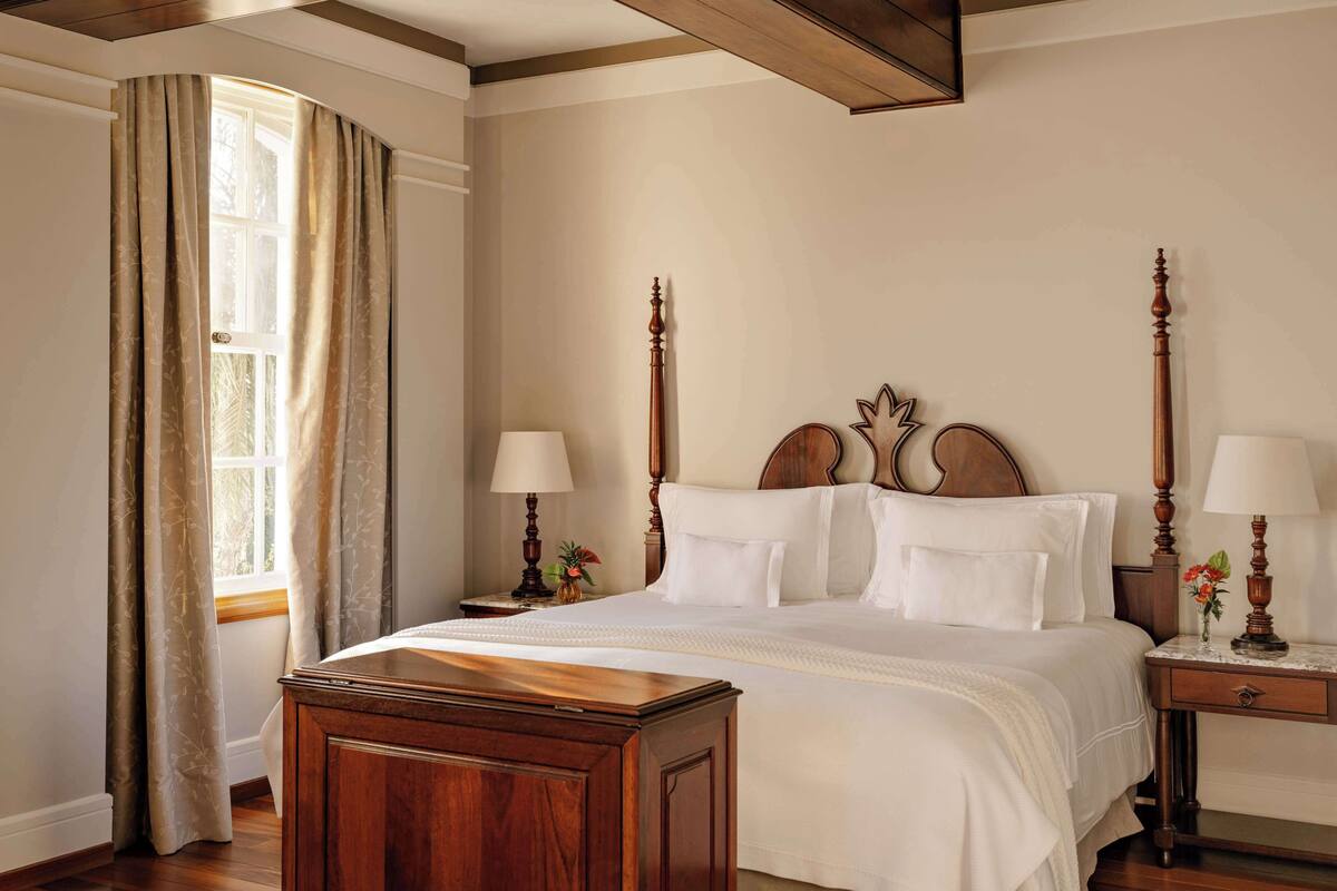 A bedroom with a large bed, wooden headboard, two bedside tables with lamps, and a wooden nightstand.