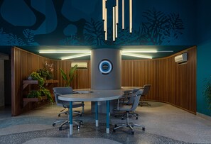 A modern conference room with a round table, four chairs, and a central column with a circular logo. - Novotel Rio de Janeiro Leme (Rio de Janeiro)
