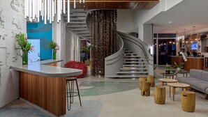 Un hall d’entrée moderne avec un escalier à volutes, un comptoir d’accueil et un espace détente doté de tables rondes en bois.
