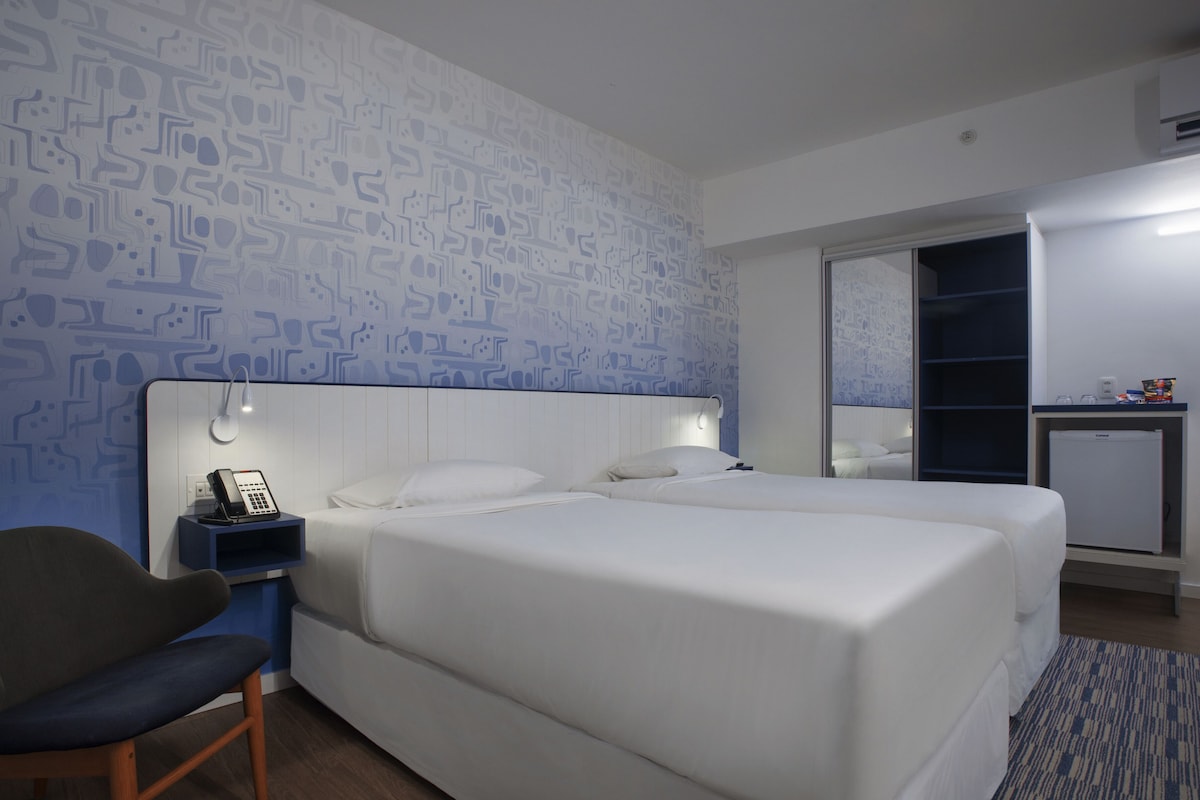 A hotel room with a large bed, a desk with a phone, a chair, and a wardrobe.