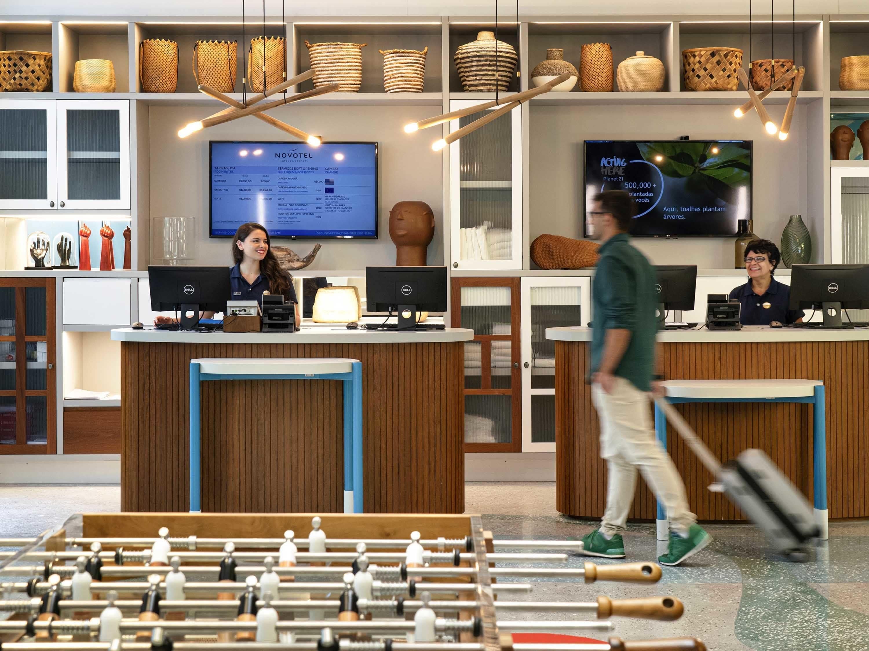 A hotel reception area with wooden reception desks, computers, and a large screen displaying hotel services.