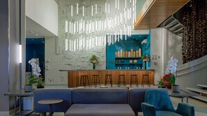 Un hall d’entrée moderne avec un canapé d’angle, un coin bar et un mur décoratif agrémenté de luminaires verticaux.