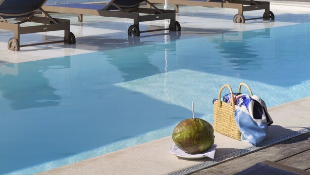Un espace aménagé au bord de la piscine, avec des chaises longues et des parasols, une noix de coco et un sac.