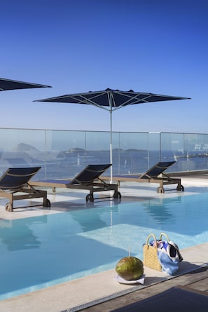 A poolside area with lounge chairs and umbrellas, a coconut, and a bag. - Novotel Rio de Janeiro Leme (Rio de Janeiro)