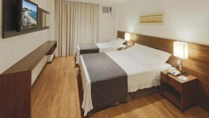 Habitación de hotel con dos camas, un televisor montado en la pared, un escritorio y una ventana con cortinas.