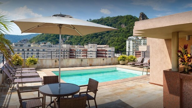 Zona de piscina en la azotea con sillones de descanso, una mesa y una sombrilla.