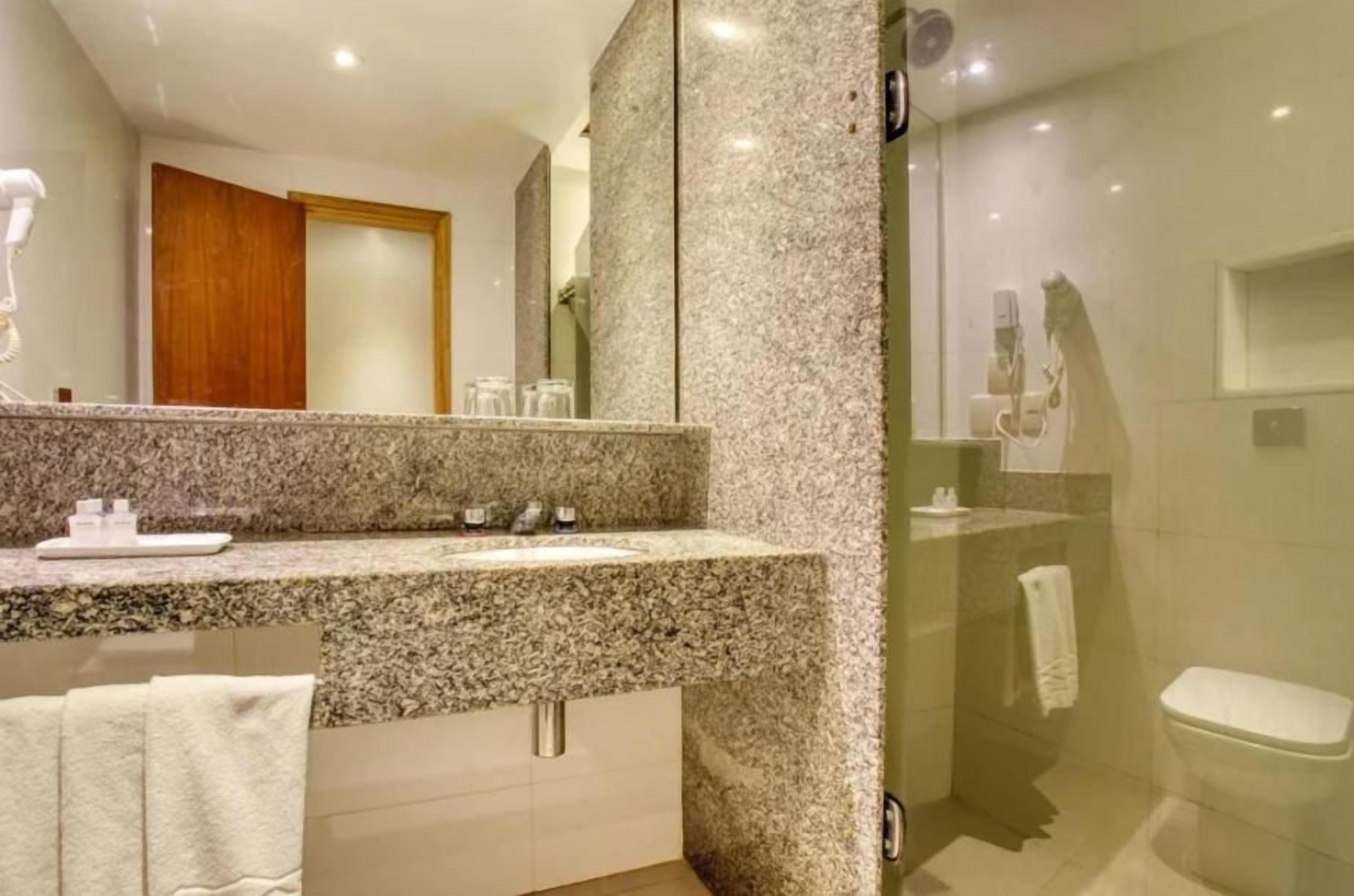 Une salle de bain moderne avec un comptoir en granit, un grand miroir et une cabine de douche en verre.