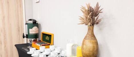 A table with a coffee maker, a box of tea, and a vase with dried plants.
