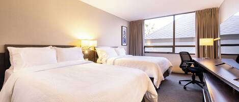 A hotel room with two beds, a desk, and a chair.