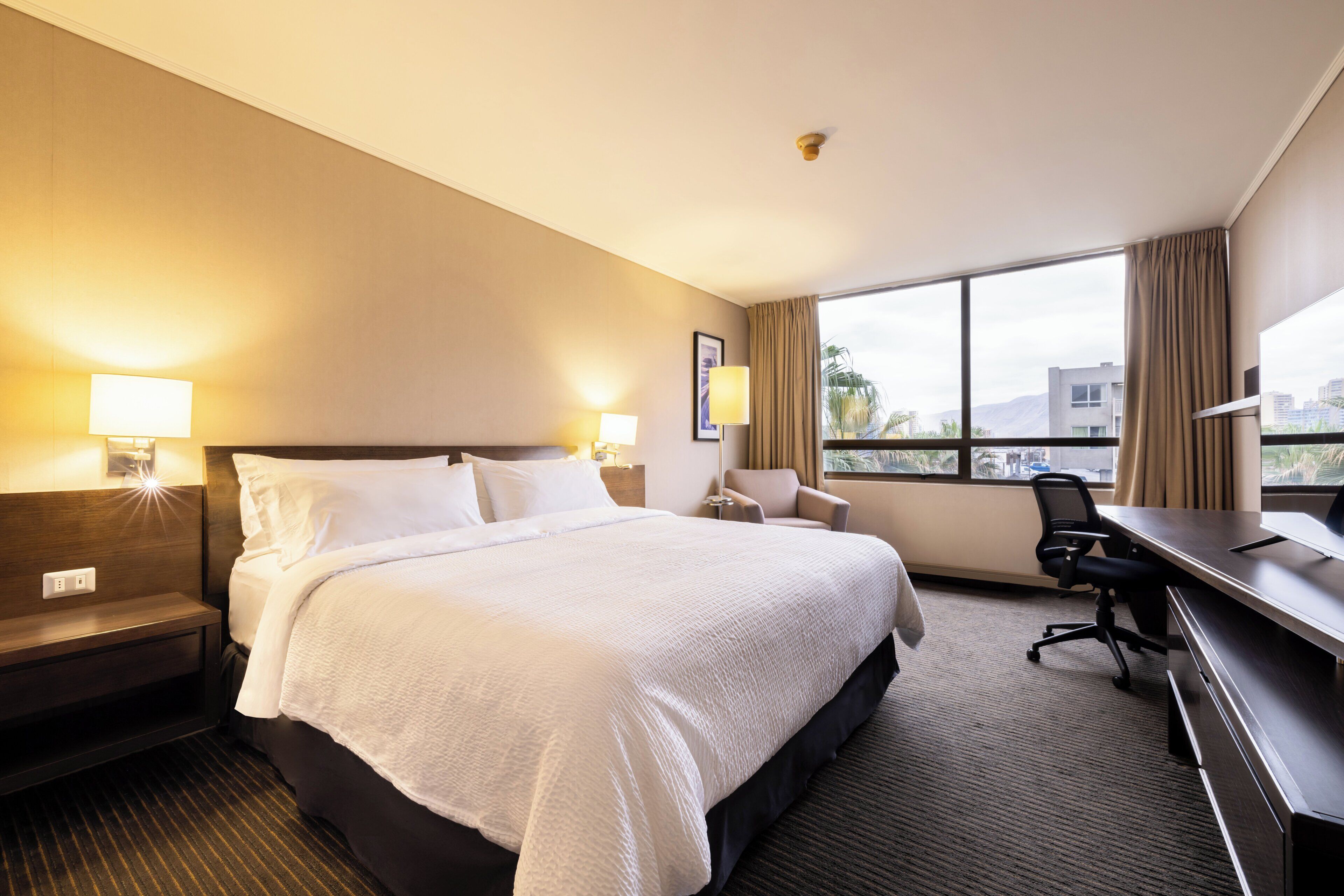 A hotel room with a large bed, a desk, a chair, and a window with a view.