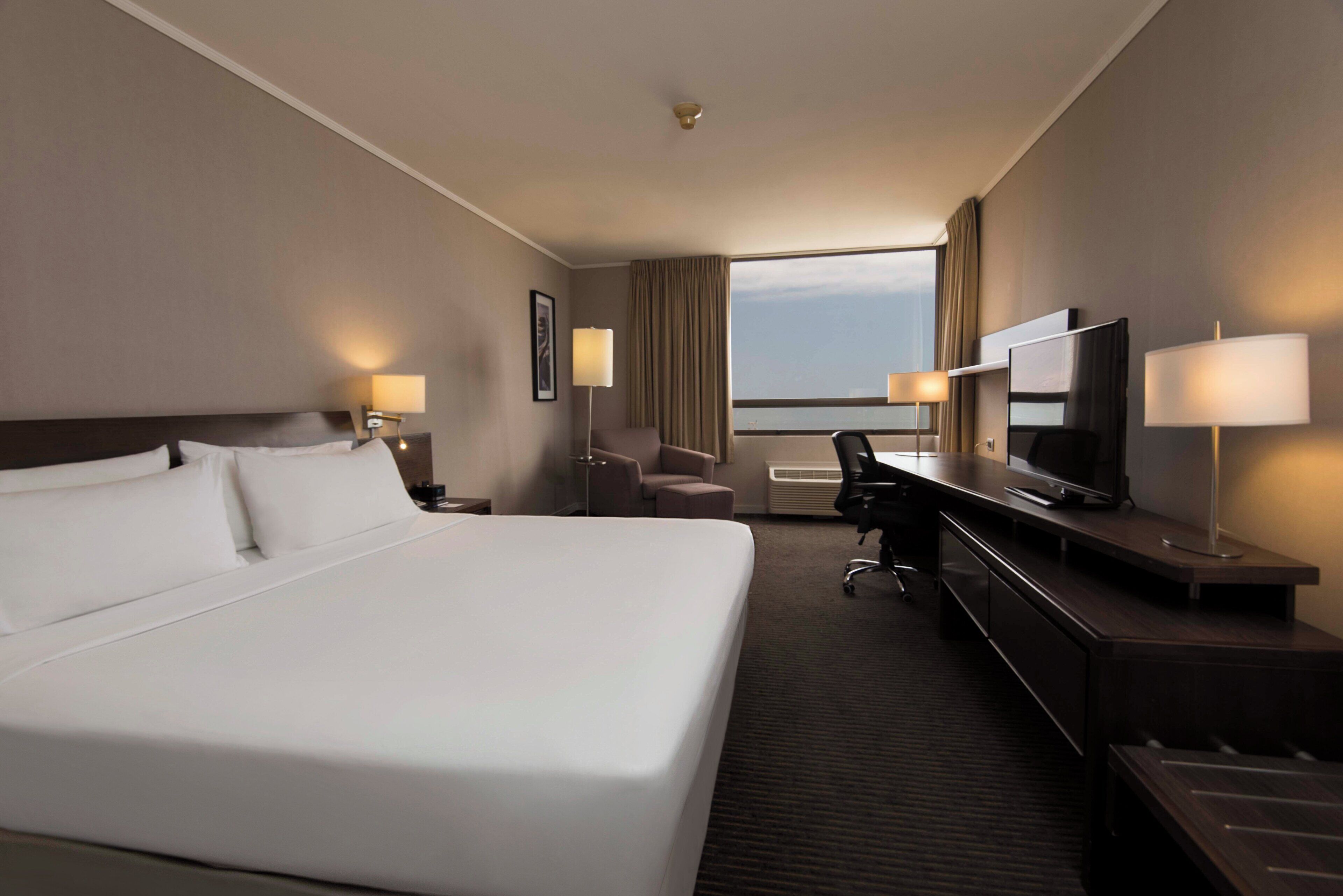 Una habitación de hotel con una cama grande, un escritorio con televisor y una silla.