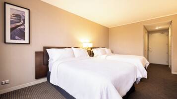 A hotel room with two beds, a nightstand, a lamp, a framed picture on the wall, and a carpeted floor.