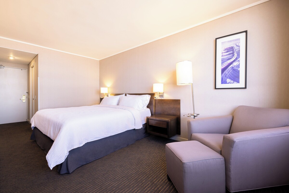A hotel room with a bed, bedside tables, a chair, and a framed picture on the wall.
